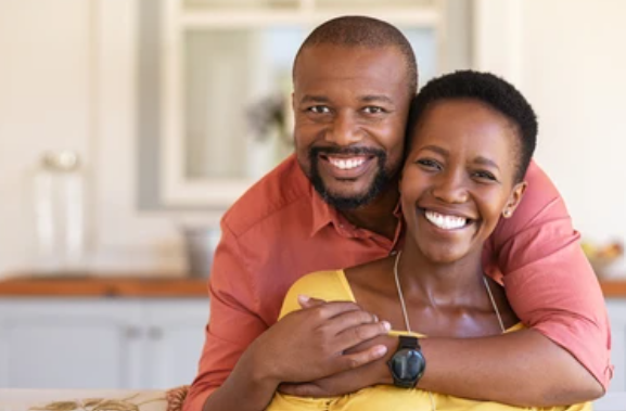 Loving couple in kitchen - man embracing woman from behind, both smiling warmly
