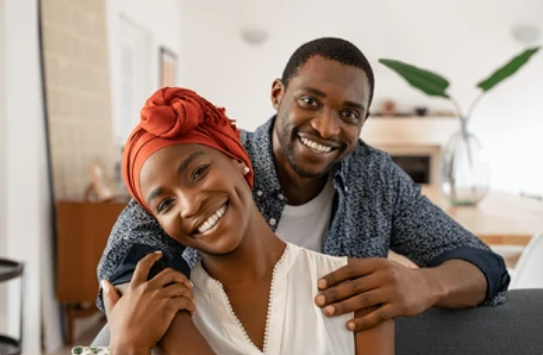 Happy couple at home - woman in red headwrap and man in gray cardigan smiling together
