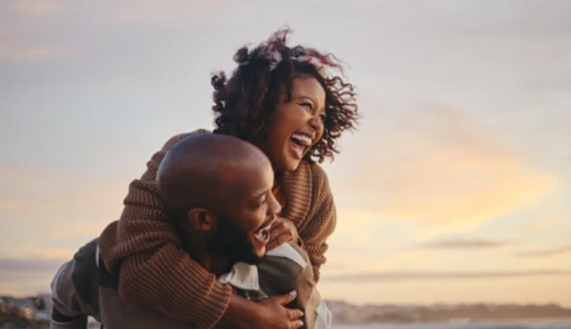 Joyful couple outdoors at sunset - man giving woman piggyback ride, both laughing