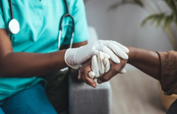 Healthcare provider in teal scrubs holding patient's hands in supportive gesture